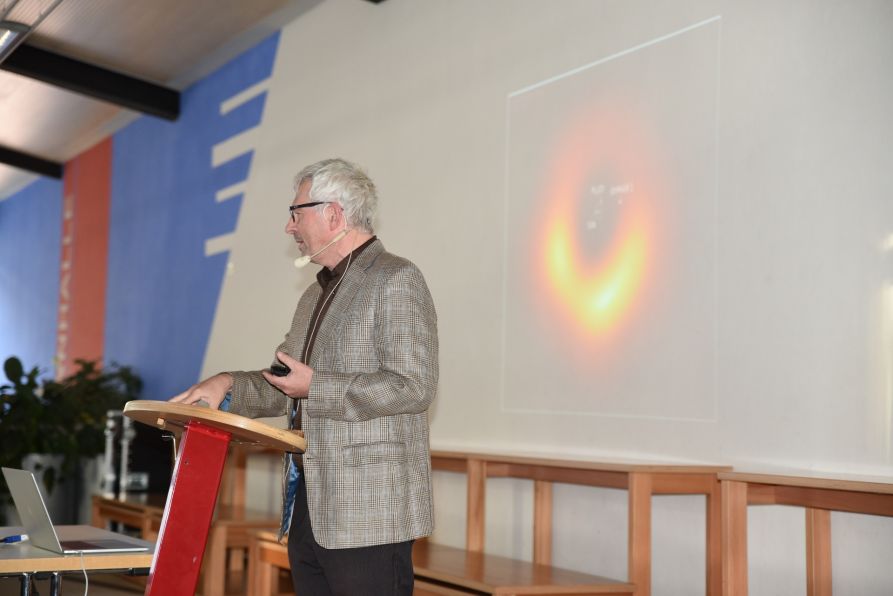 Prof. Dr. Andreas Burkert bei seinem Vortrag vor der Projektion eines Schwarzen Lochs