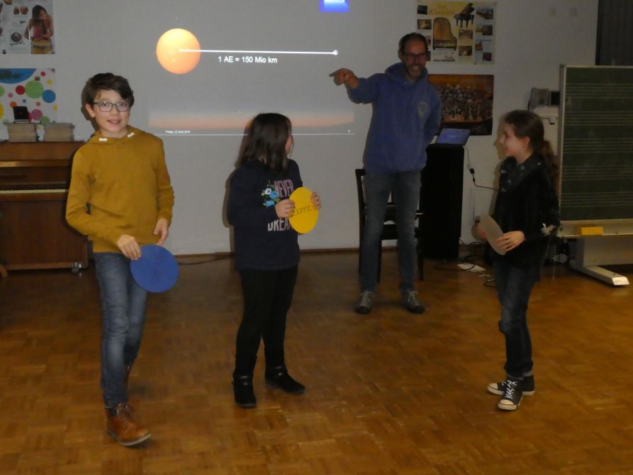 Drei Schüler demonstrieren die Rotation von Erde und Mond um die Sonne.
