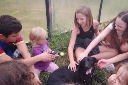 Hofhund Wally im Kreis der Schüler:innen zusammen mit dem jüngsten Nachwuchs am Hof
